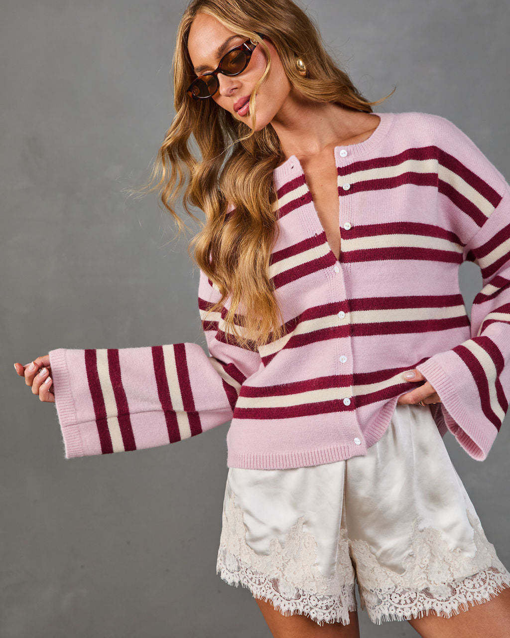 Women's striped pink burgundy knit cardigan with bell sleeves and white buttons, styled with cream lace shorts