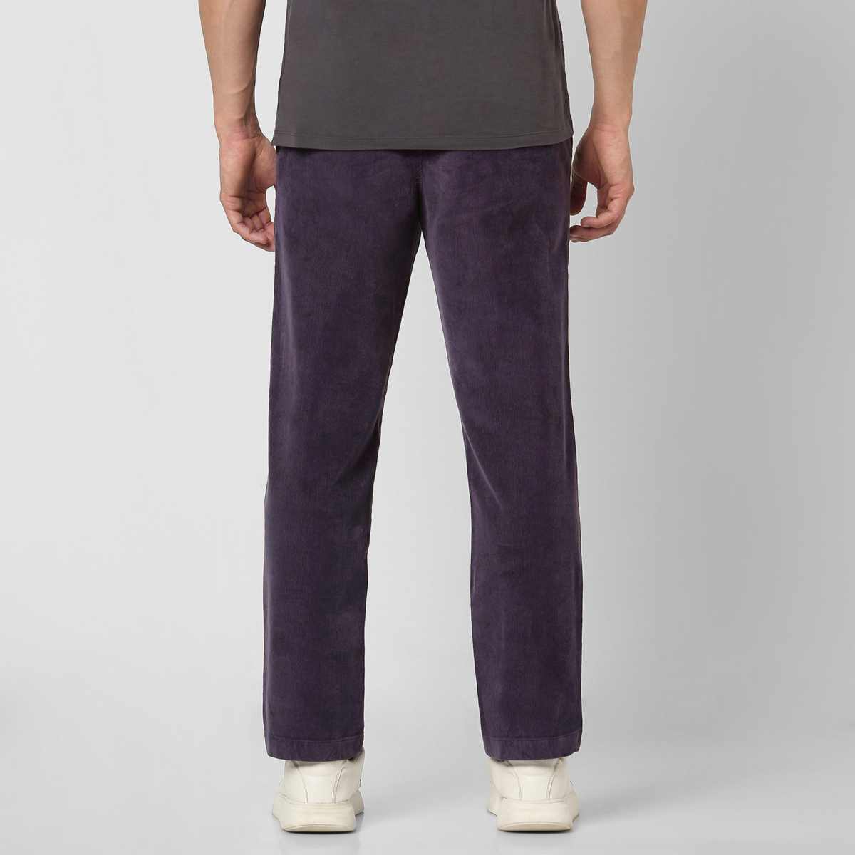 A person wearing Corduroy Easy Pant in dark purple cotton corduroy and white sneakers stands with their back to a plain light gray background—an ideal addition to your stylish fall and winter wardrobe.