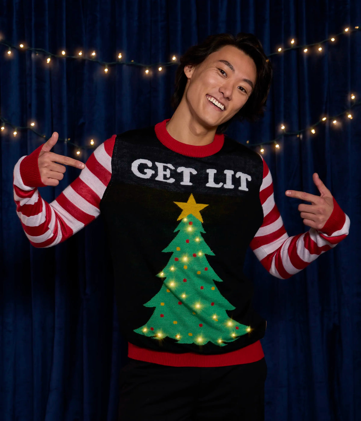Person wearing a festive sweater with a Christmas tree and 'GET LIT' text, pointing at the sweater.