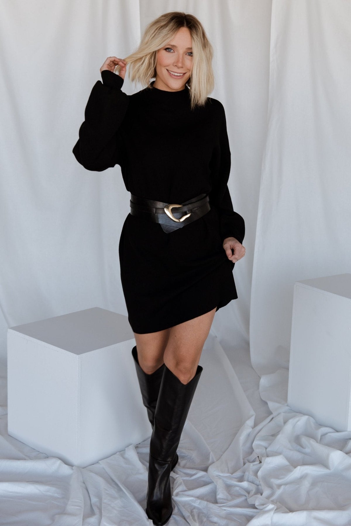 Three-quarter view of black knit sweater dress showing straight silhouette, short hemline, and textured knit across the body for everyday wear.